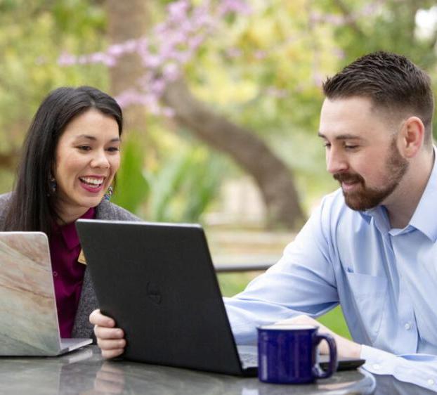 Two people with laptops talk and work outside on a nice day