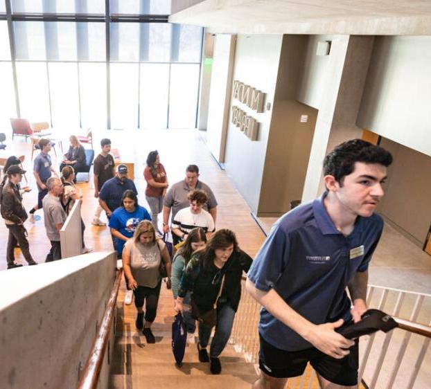 A student leading a campus tour group up the stairs of the library