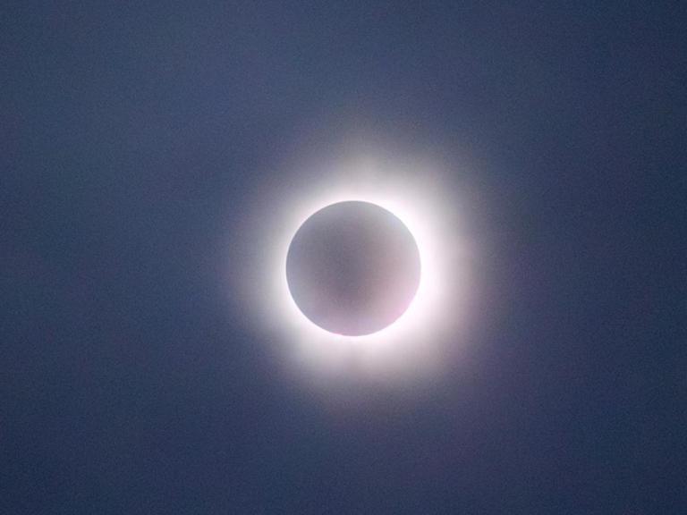 这张照片拍摄的是日全食, where the moon completely covers the sun, 只留下明亮的日冕，在黑暗的圆盘周围形成一个发光的环. 天空变暗，增加了日食的戏剧性效果. The soft, 日冕发出的光芒与月亮的阴影形成了鲜明的对比, 这是对自然天体事件的迷人描绘.