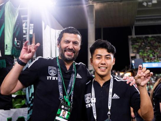 校友 on staff with Austin FC make toppers up hand signs at an Austin FC game.